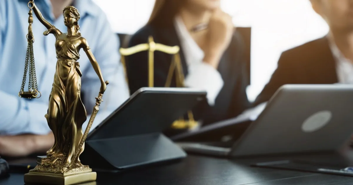 Lady Justice statue with blurred attorneys working on laptops in office