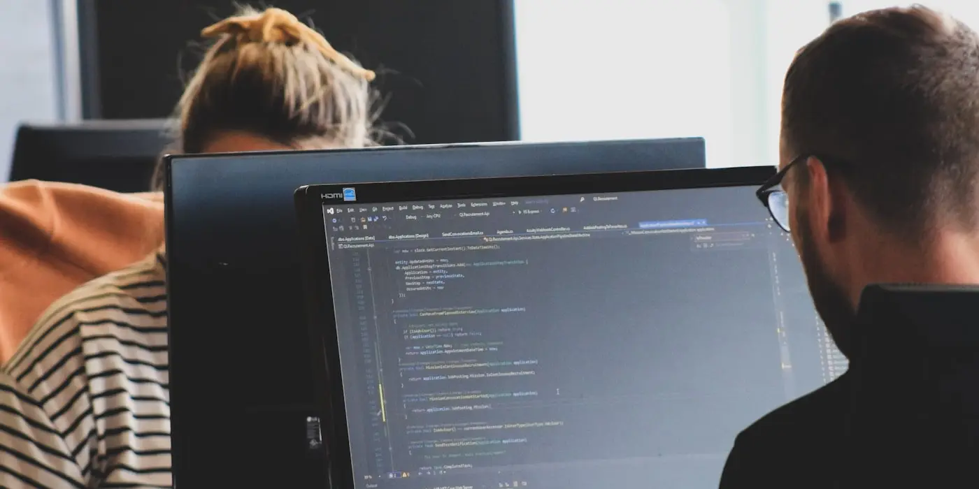 Two developers working through code on adjacent monitors